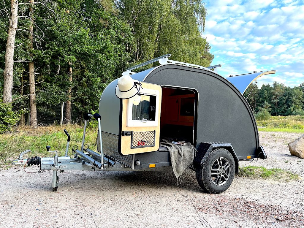 Minicamper steht am Waldrand in einem sonnigen Tag.